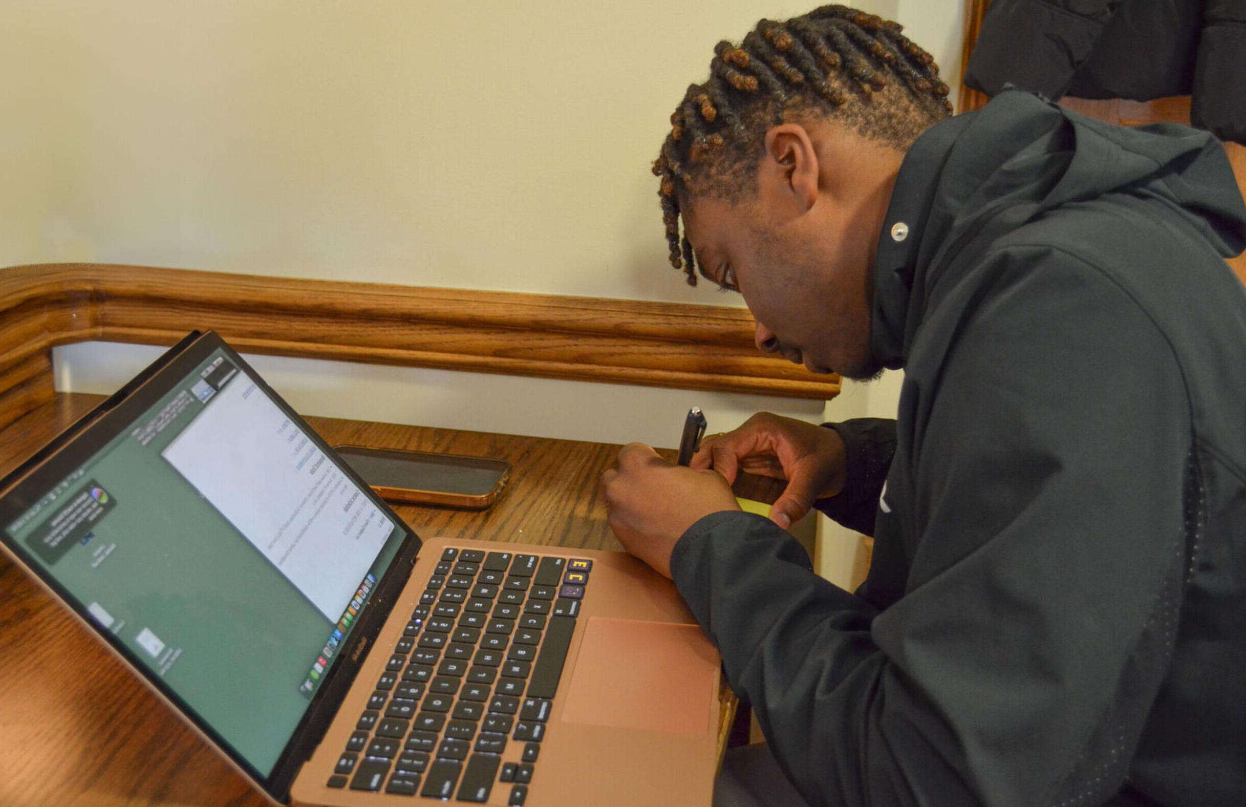 一名男学生在宿舍的桌子上用笔记本电脑写笔记