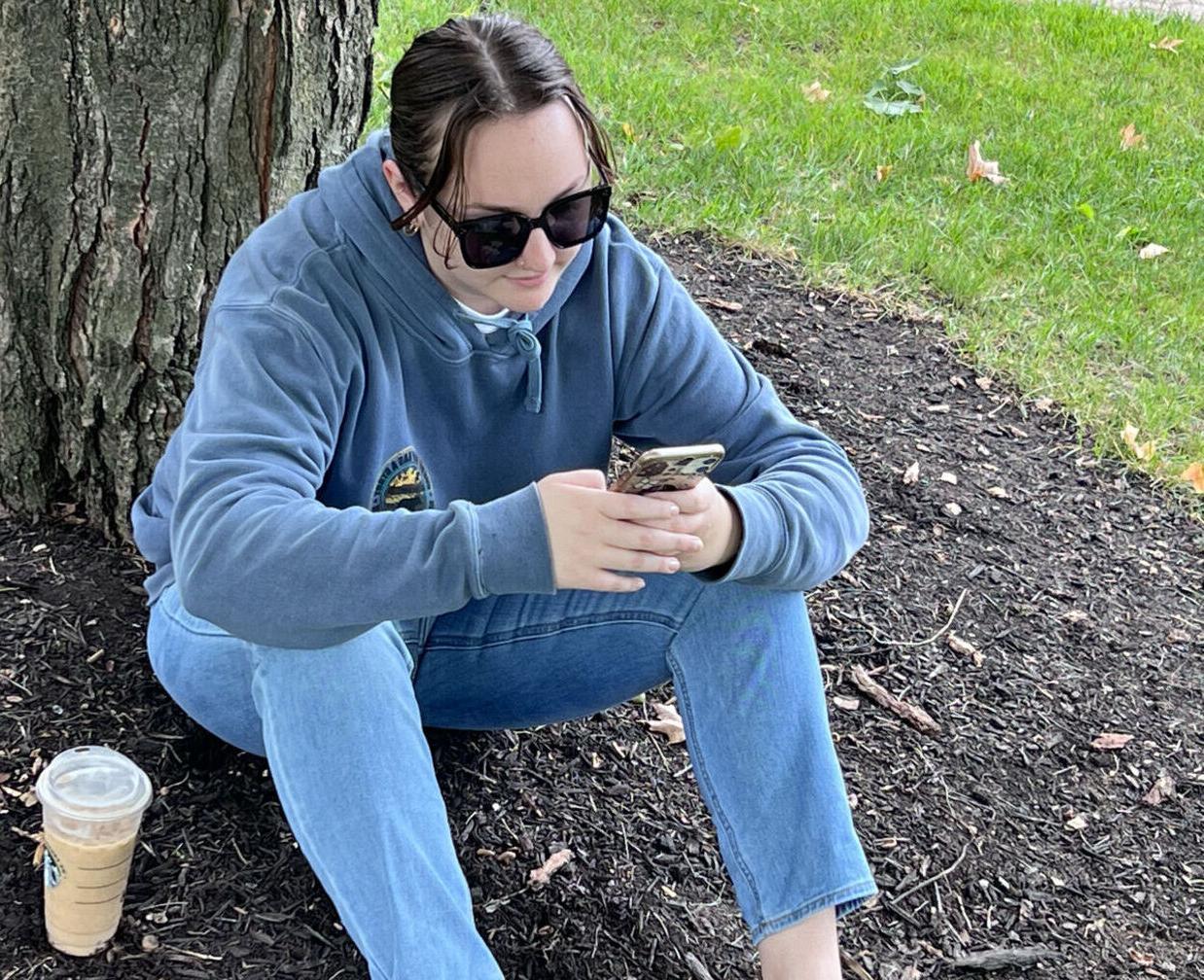 一名学生坐在校园的树下看手机